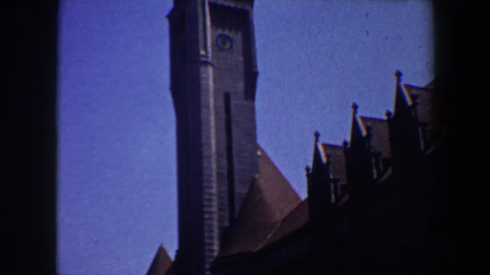 1964 Saint Louis 8mm frame showing the grey belltower, clock face, blue sky, and heavy dark edge from the scanned film frame.
