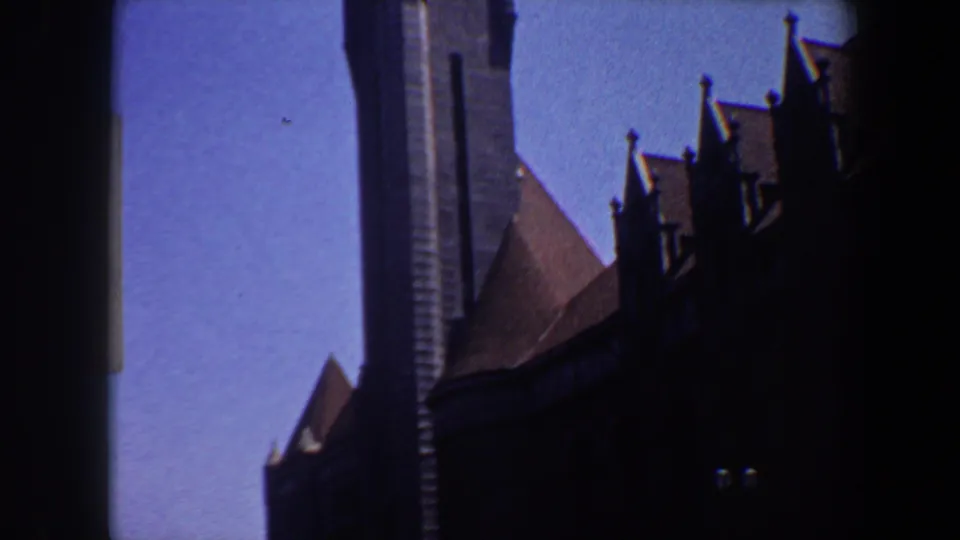1964 Saint Louis 8mm frame showing a dark, castle-like church exterior with a tall tower, steep roof, and blue sky.