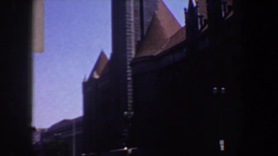 1964 Saint Louis 8mm frame showing the church exterior in shadow, with a tower, steep roofline, and small trees below.