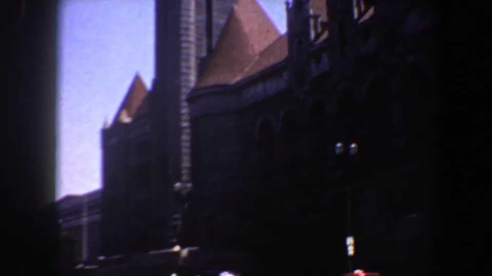 1964 Saint Louis frame of a large Gothic-style church exterior, with dark stonework, steep roofs, and a bright blue sky.