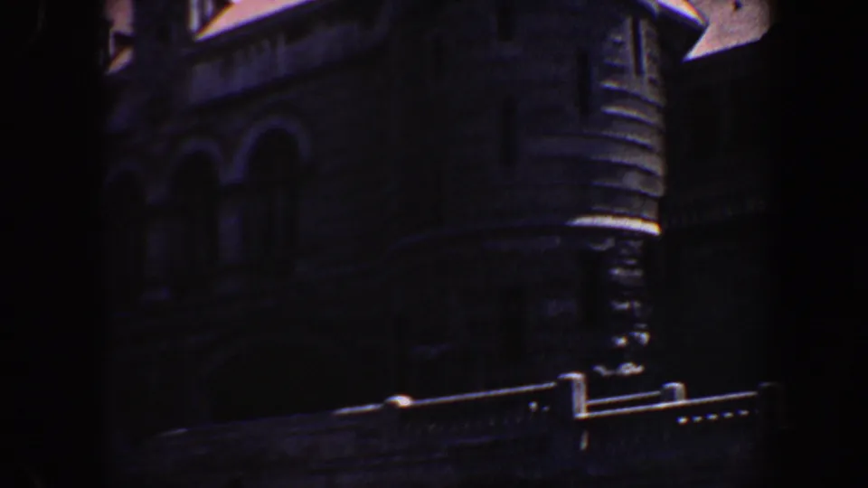 The camera pans along the Saint Louis building exterior, showing dark masonry, arched openings, and a steep roof edge.