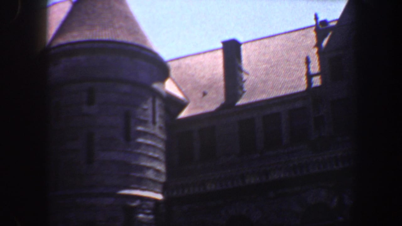 Ornate stone building facade with turret and steep roof, partly framed by dark vertical edges.
