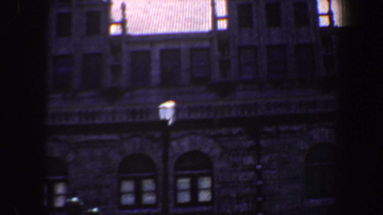 Dark-framed view of a stone building with arched windows and a streetlamp.