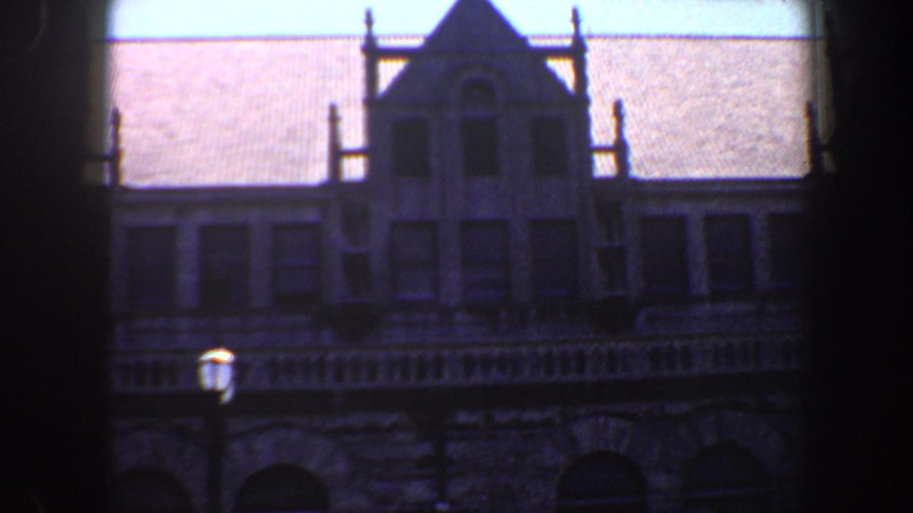 Gabled roofline and upper windows of a stone building behind a dark vertical frame.