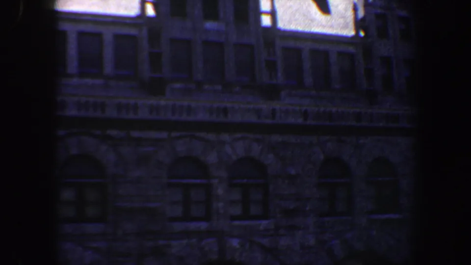 1964 Saint Louis 8mm frame showing a dim stone building facade with arched lower windows and shadowed vertical framing.