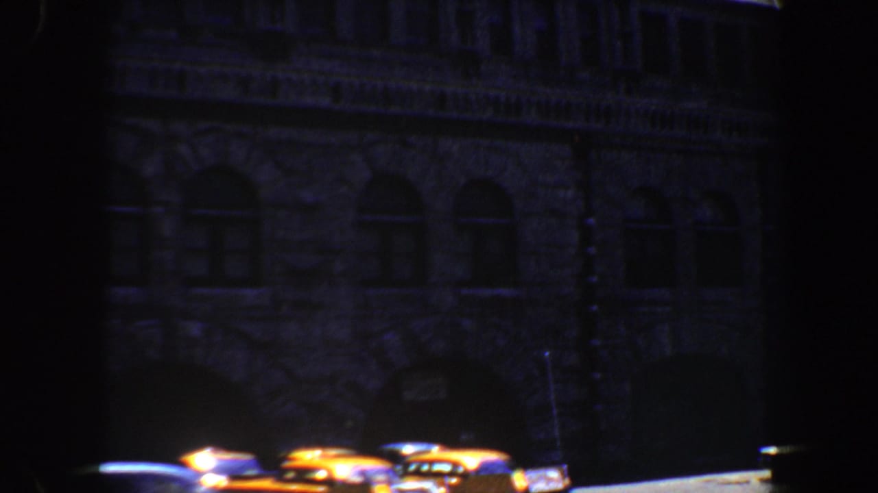 Dark stone building facade with a bright street edge and parked cars near the bottom.