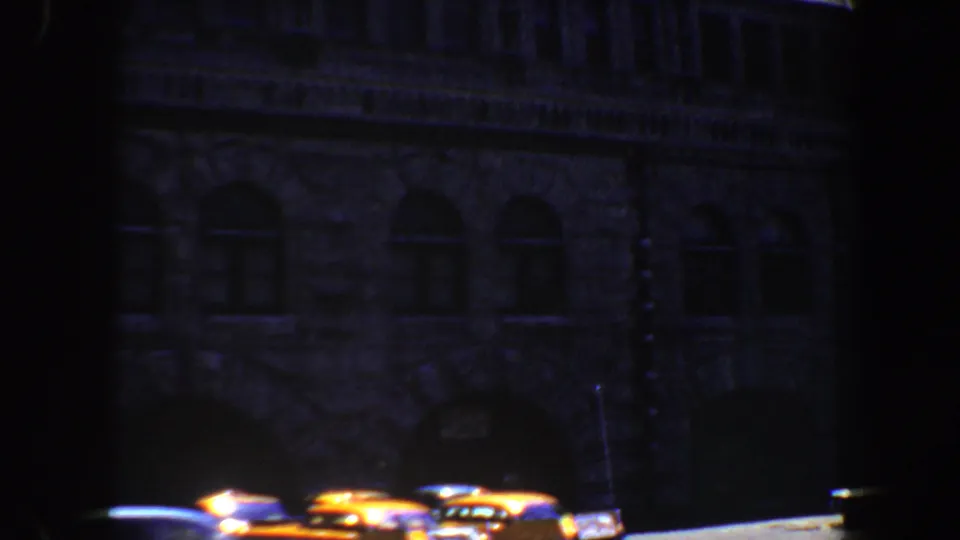 1964 Saint Louis 8mm frame with a shadowed masonry facade, arched windows, bright curb line, and several parked cars.
