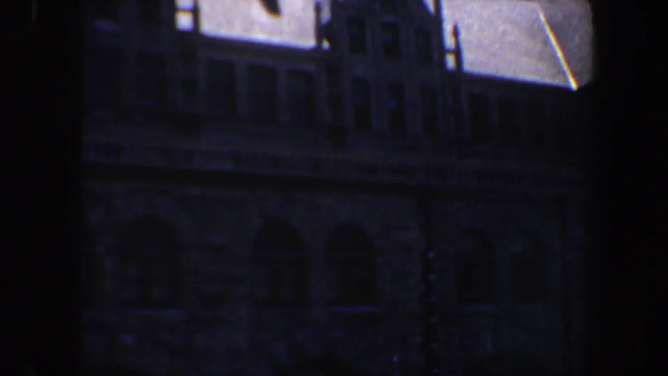 1964 Saint Louis 8mm frame looking through a dark opening toward a stone building with upper windows and arched lower openings.