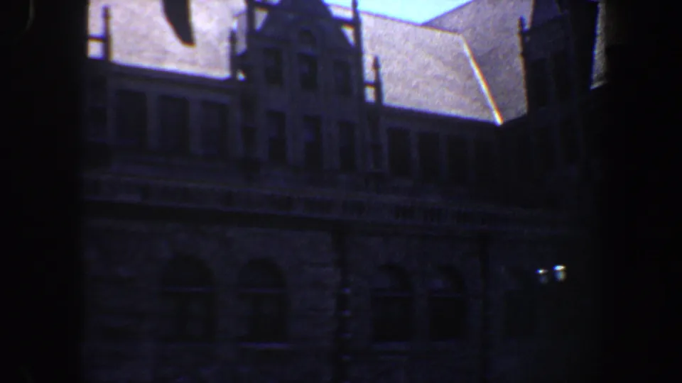 1964 Saint Louis 8mm frame of a darkened architectural exterior, with stone masonry, arched windows, and a bright sloped roofline area.