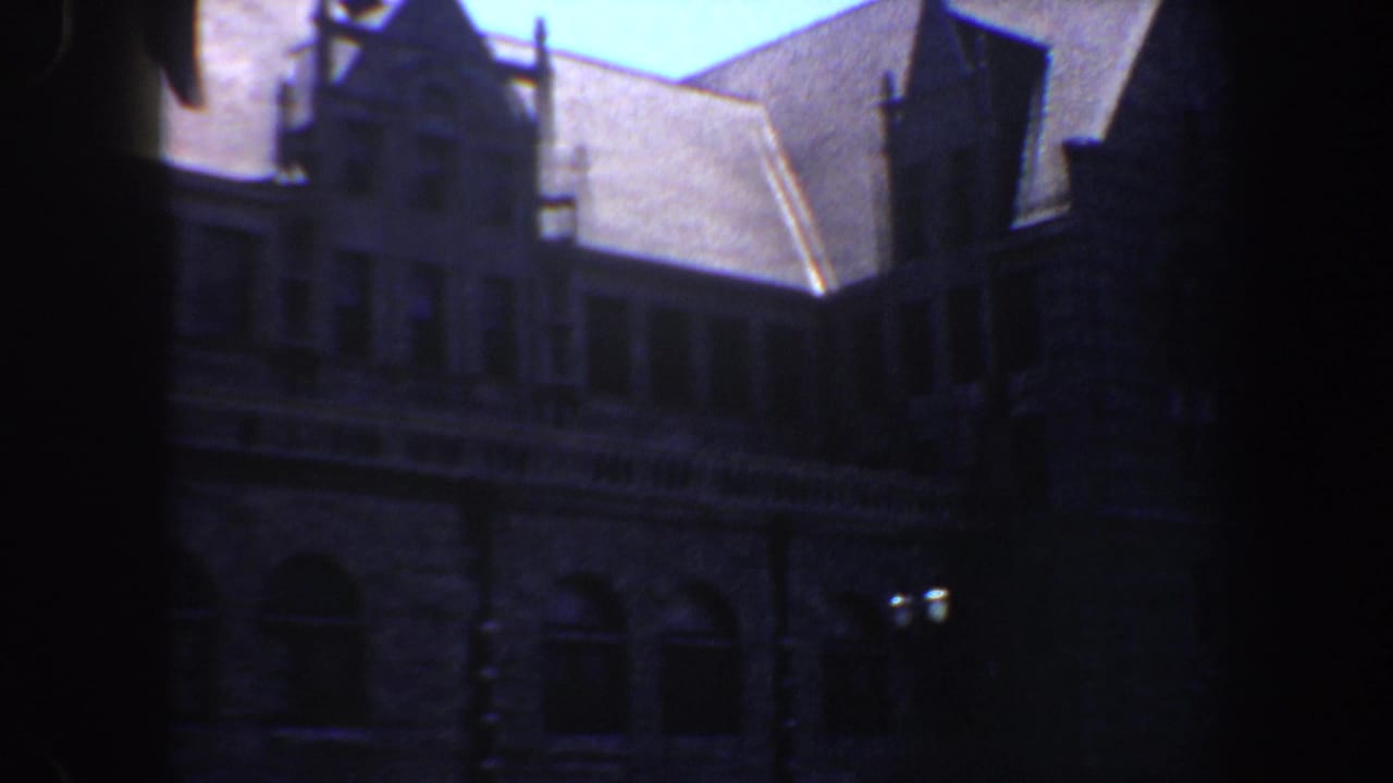 1964 Saint Louis 8mm frame showing a shadowed Gothic Revival style stone building viewed from the street below.