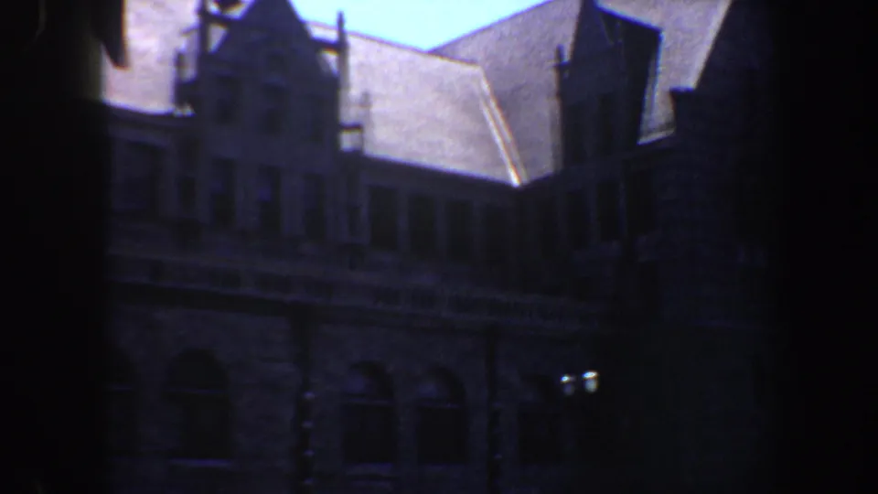 1964 Saint Louis 8mm frame showing a shadowed Gothic Revival style stone building viewed from the street below.