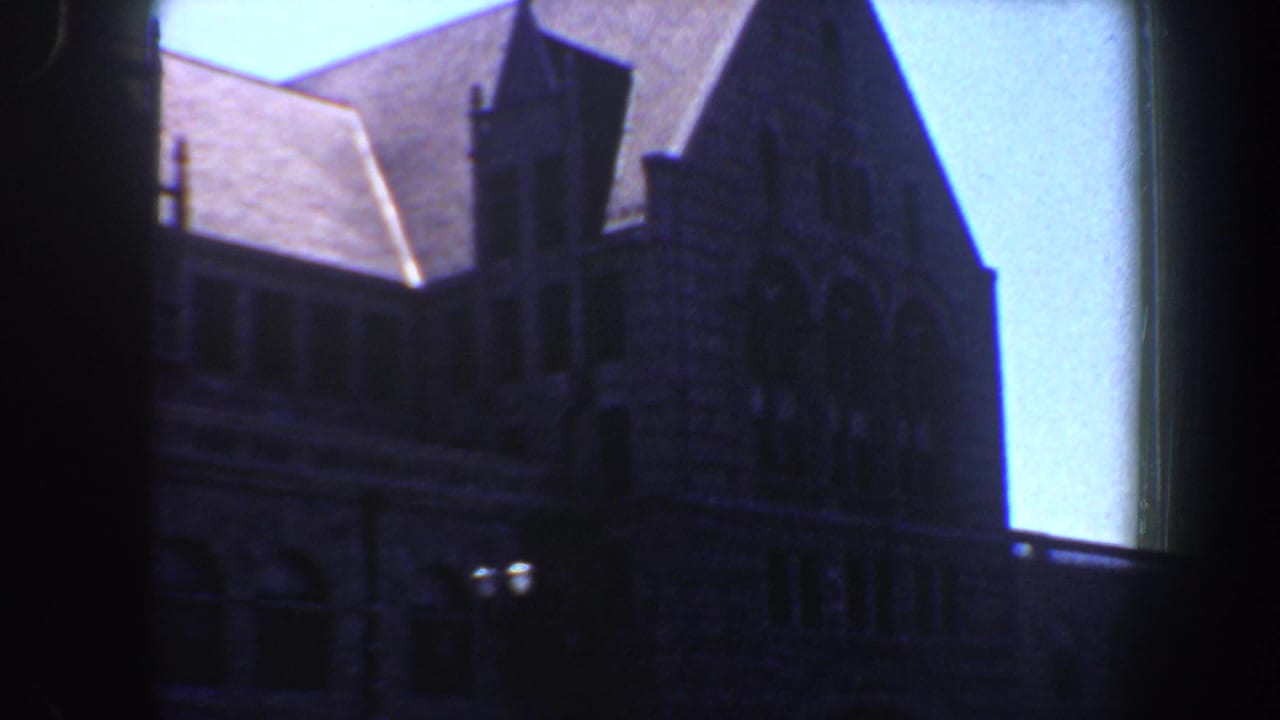Large stone building facade with roof peaks, arched details, and bright blue sky.