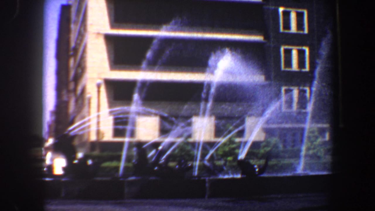 Water sprays across a fountain basin in front of a tiered building facade.