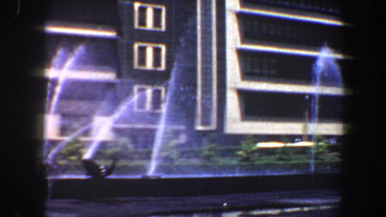Night view of a lit building facade with fountain spray in the foreground.