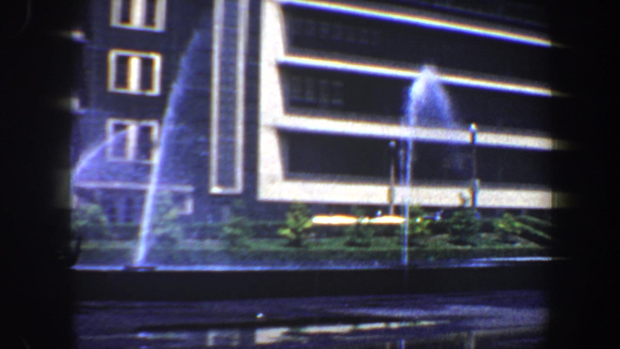 Building exterior with fountain spray and landscaping at night.