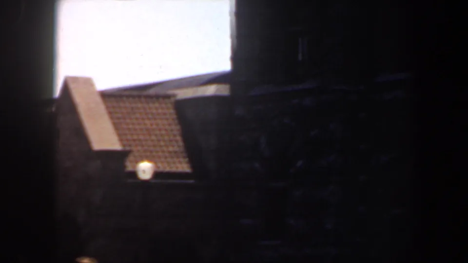 1964 Saint Louis 8mm frame with a tiled roof peak, dark building mass, and bright overexposed sky near the end of the pan.
