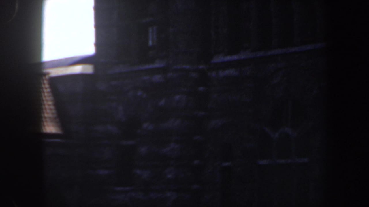 1964 Saint Louis 8mm frame showing a dim stone facade with masonry texture and a bright upper-left window area.