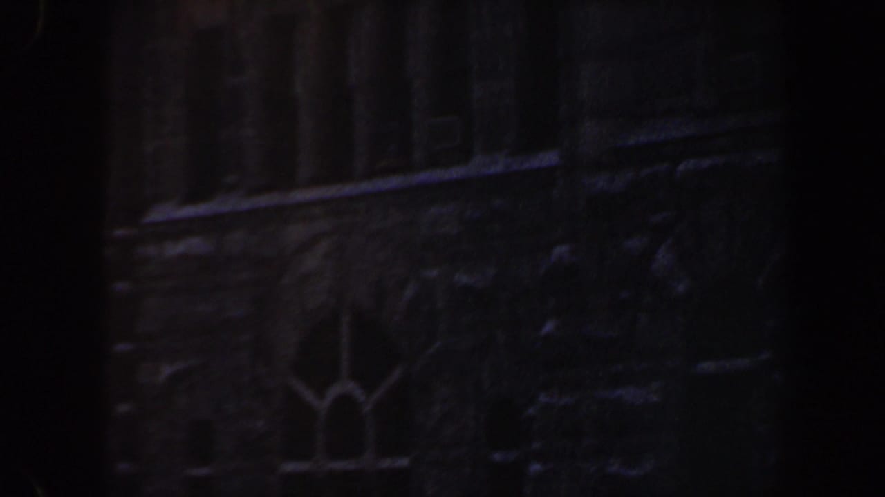 Upper portion of a dark stone building with arched window details and heavy shadows.