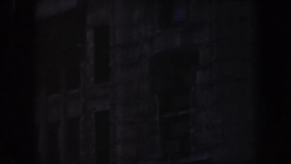 1964 Saint Louis 8mm frame showing a shadowed lower facade with faint windows and textured stonework.
