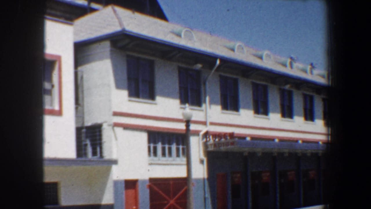 White stadium facade with rows of dark windows and red entrance details.
