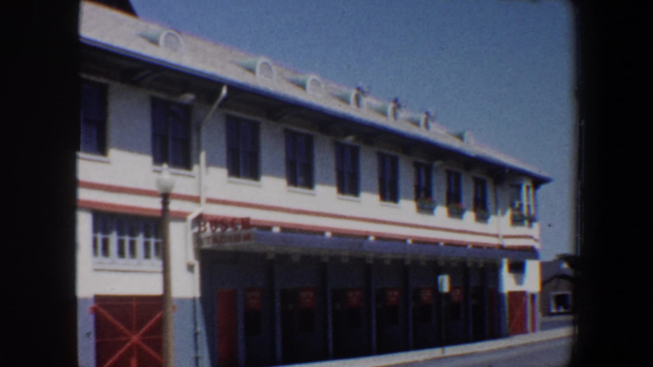 White stadium-side building with red trim, red doors, and a streetlamp in front.