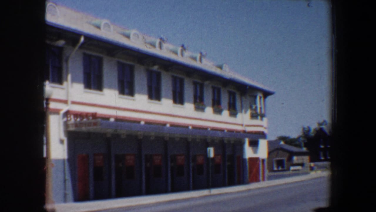Stadium frontage with multiple red doors, upper windows, and road at right.