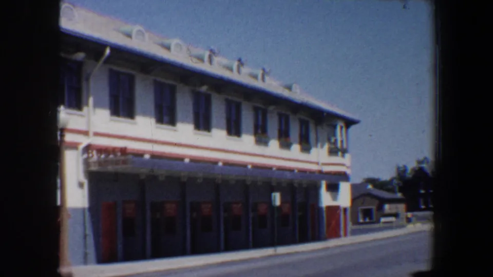 1964 Saint Louis stadium exterior with red-trimmed facade, rows of windows, red doors, and a quiet road beside it.