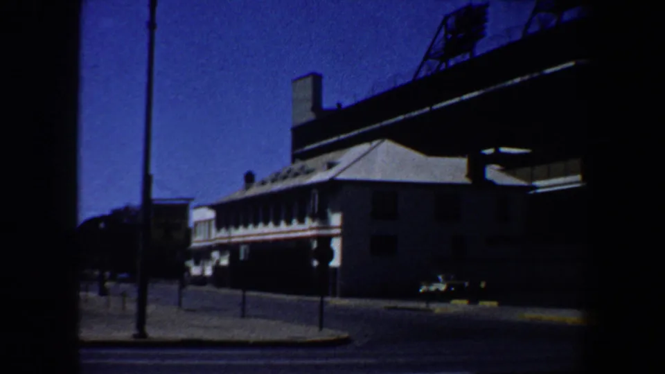 1964 Saint Louis street view near the stadium, showing an elevated structure, parked cars, a streetlamp, and a shaded building.