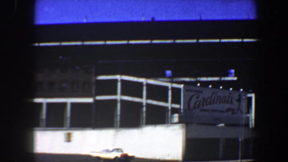1964 Saint Louis 8mm frame showing the Cardinals sign on the stadium exterior, with white wall sections and a parked car below.