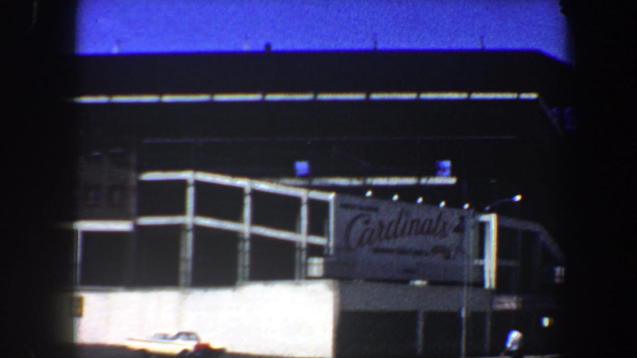 1964 St. Louis street view of a large multi-level complex with a Cardinals sign and a car along the lower roadway.
