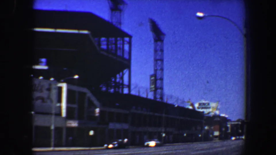 The camera looks down a St. Louis roadway beside the large complex, with cars, a light pole, and upper structural framing visible.