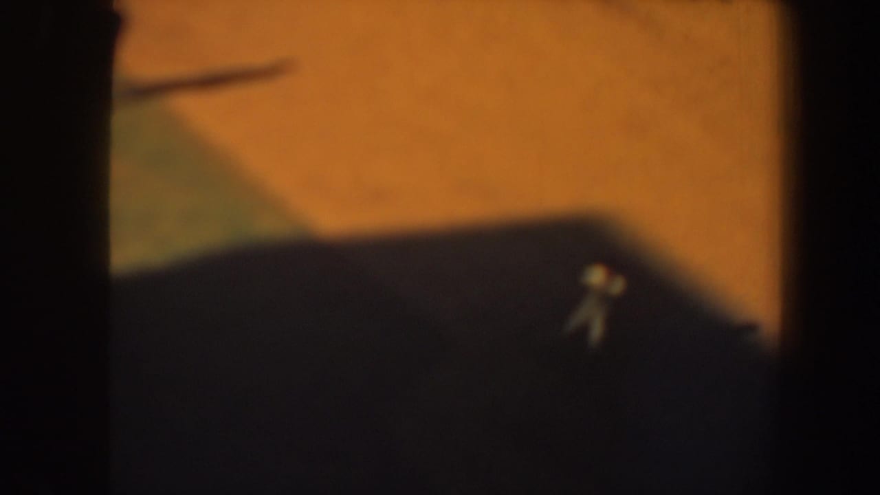 Small baseball player on a darkened portion of the field near grass and dirt.