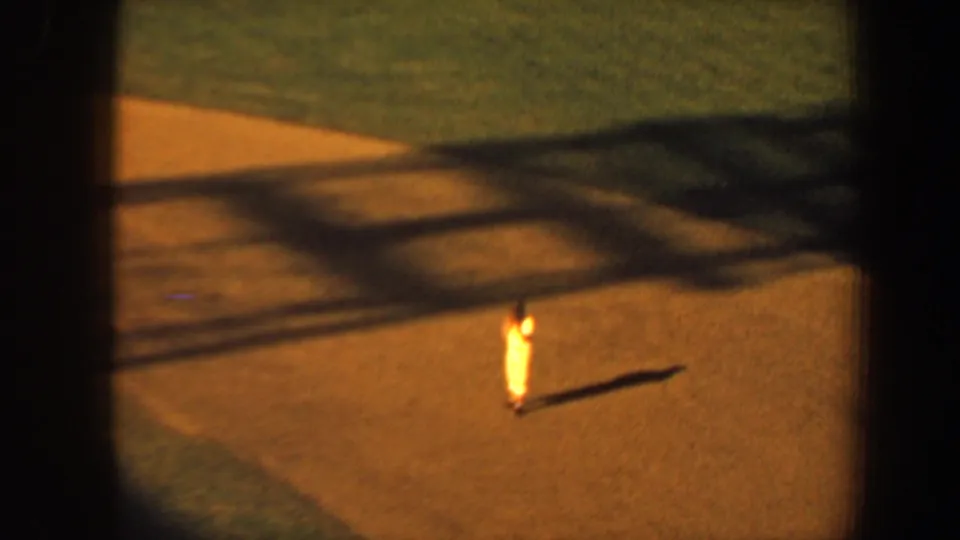 1964 Saint Louis 8mm frame showing a bright uniformed player standing on sunlit dirt, with grass and long afternoon shadows nearby.