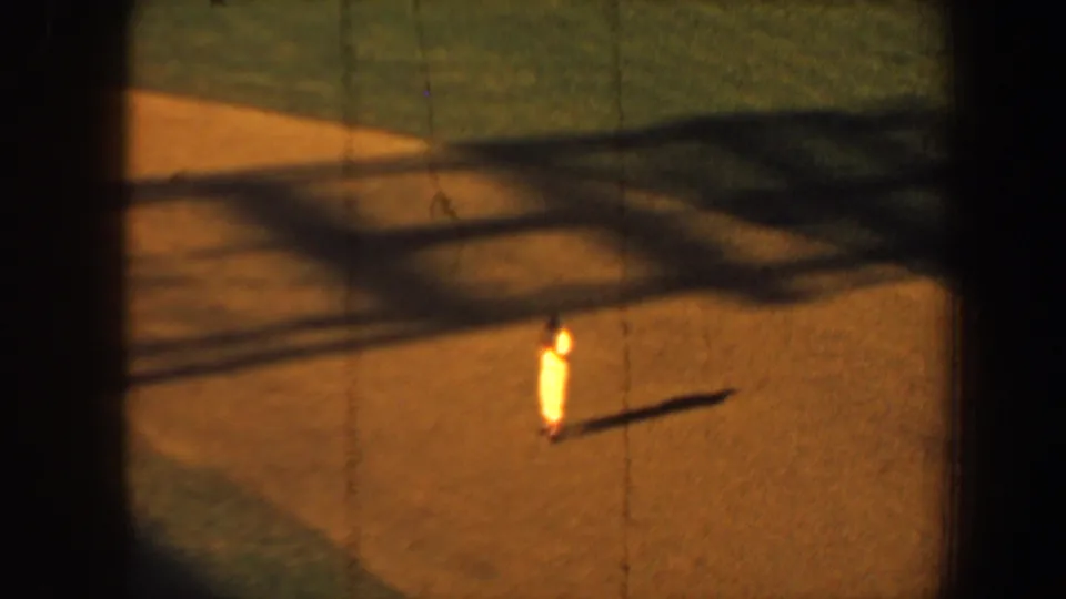 1964 Saint Louis home-movie frame with a lone bright-clad baseball player on the dirt, surrounded by dark borders and broad field shadows.