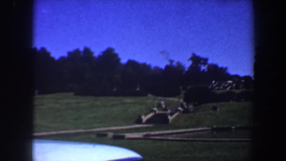 1964 Saint Louis 8mm view of a landscaped lawn and walkway, with a curved water edge and heavy film-frame shadows.