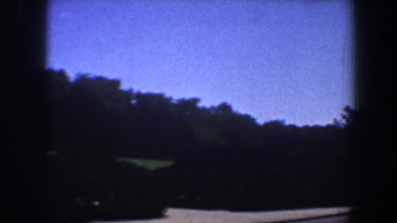 1964 Saint Louis 8mm frame with blue sky, trees, lawn, and a curved path during the pan toward the church.