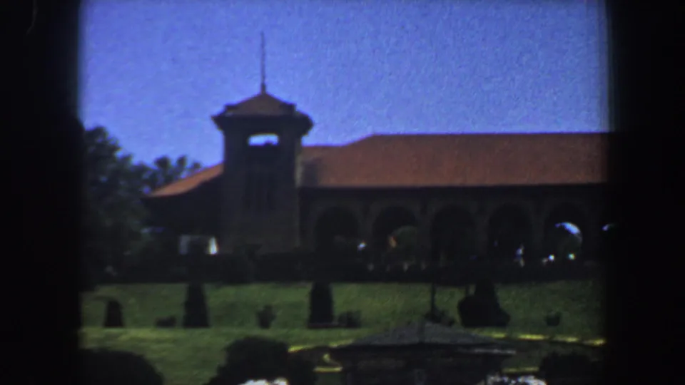 1964 Saint Louis frame showing a church exterior with bell tower, red-tiled roof, arched facade, and landscaped lawn.