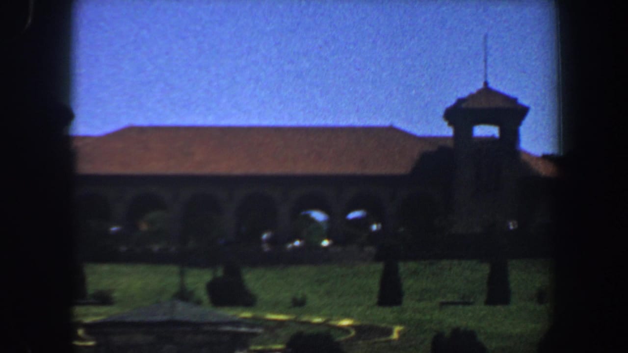 Arched building with tower behind a grassy lawn under a blue sky.