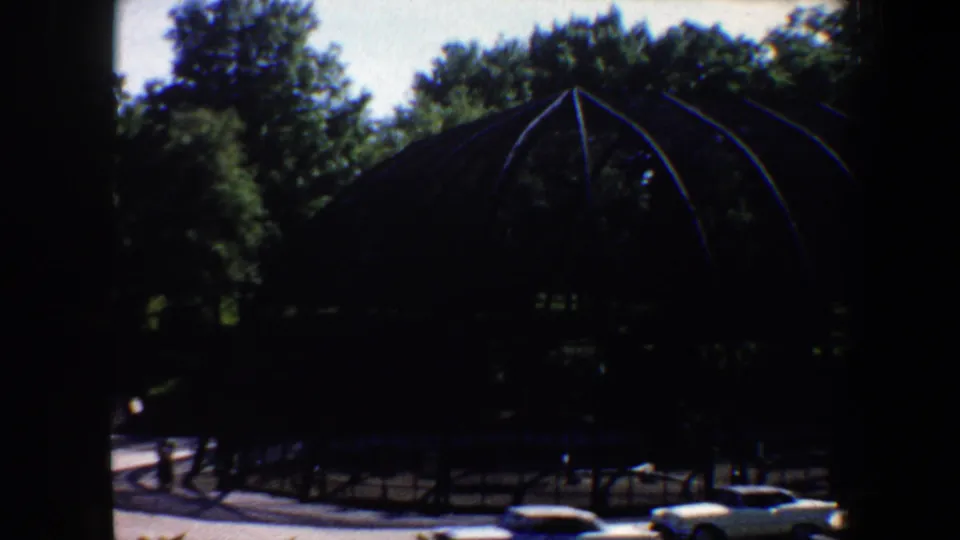 A wider 1964 Saint Louis zoo view shows a large arched aviary structure in shade with trees and cars nearby.