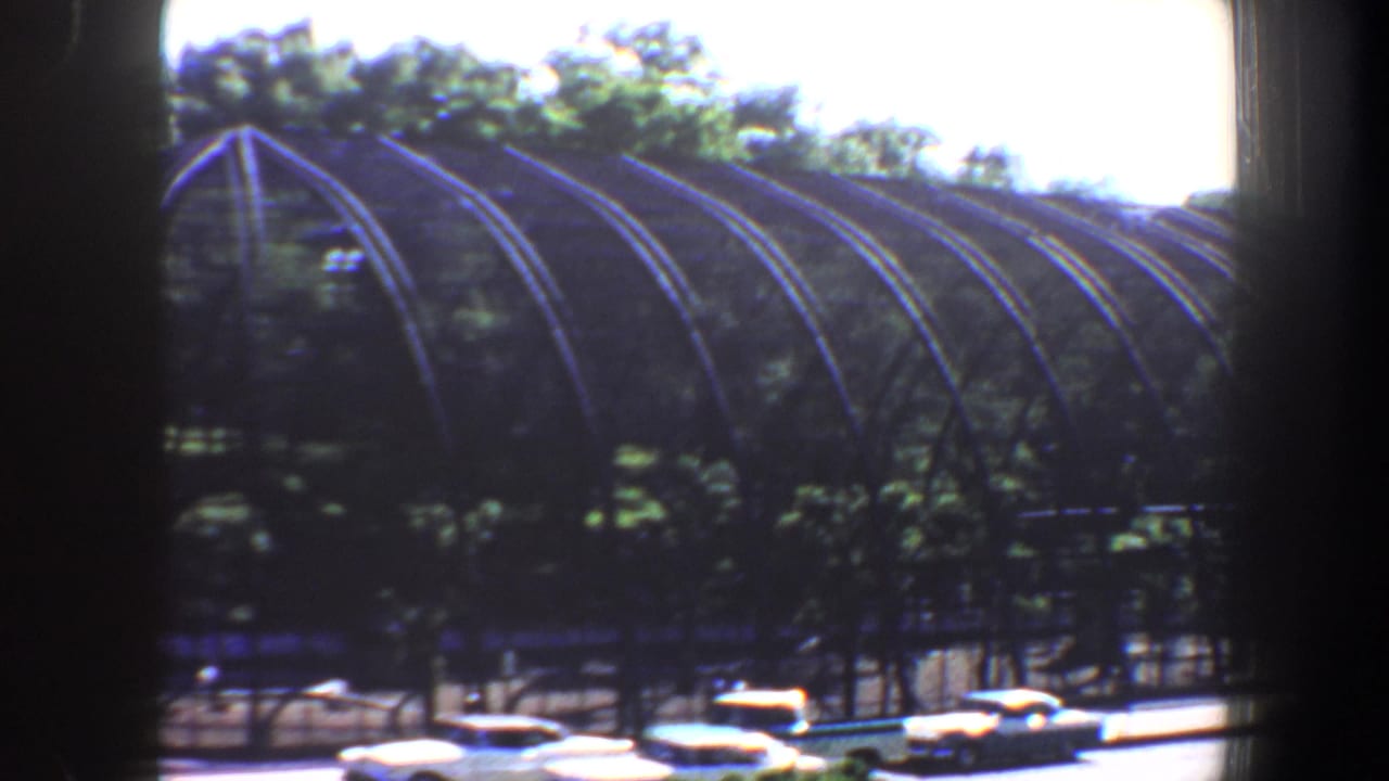 Large arched garden structure partly shaded by trees with cars below.