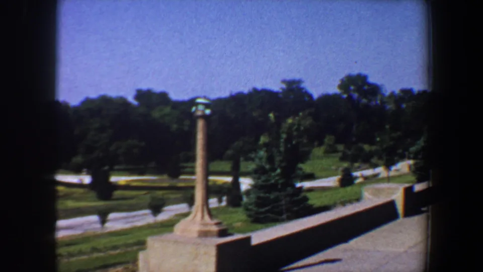 1964 view across Saint Louis garden park landscaping, with a pillar in the foreground, curving paths, lawns, and trees.