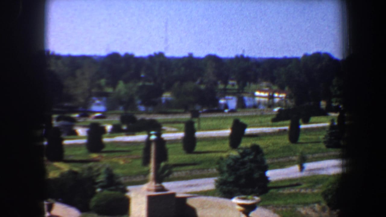 Curved roads and clipped plantings lead across a landscaped park with water and trees beyond.