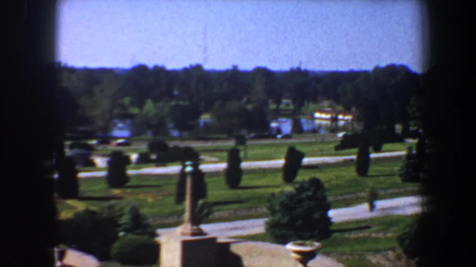 Saint Louis park landscape circa 1964 with winding drives, clipped hedges, stone posts, green lawns, distant water, and trees.