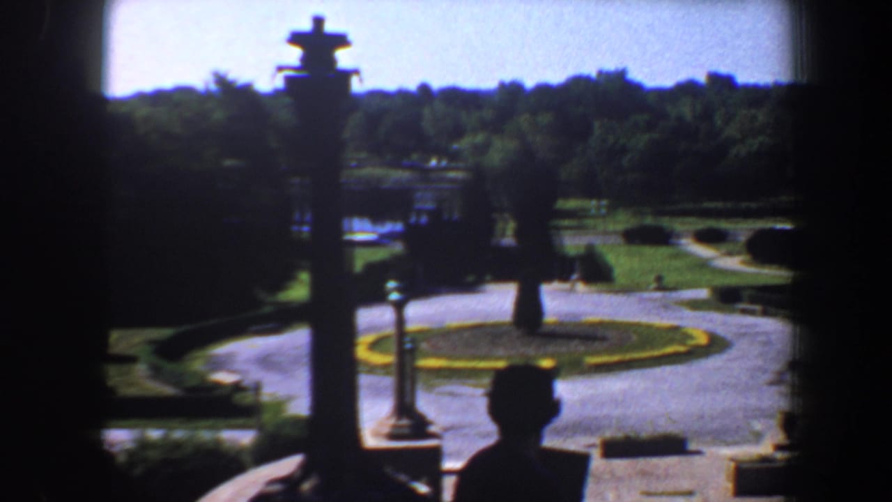 Circular driveway and formal garden seen from a shaded entrance with a small silhouetted figure.
