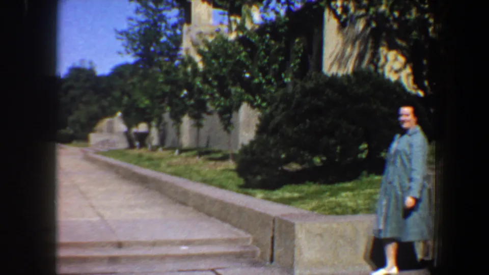 A woman in light blue stands near the edge of a stone walkway in 1964 Saint Louis estate garden footage.