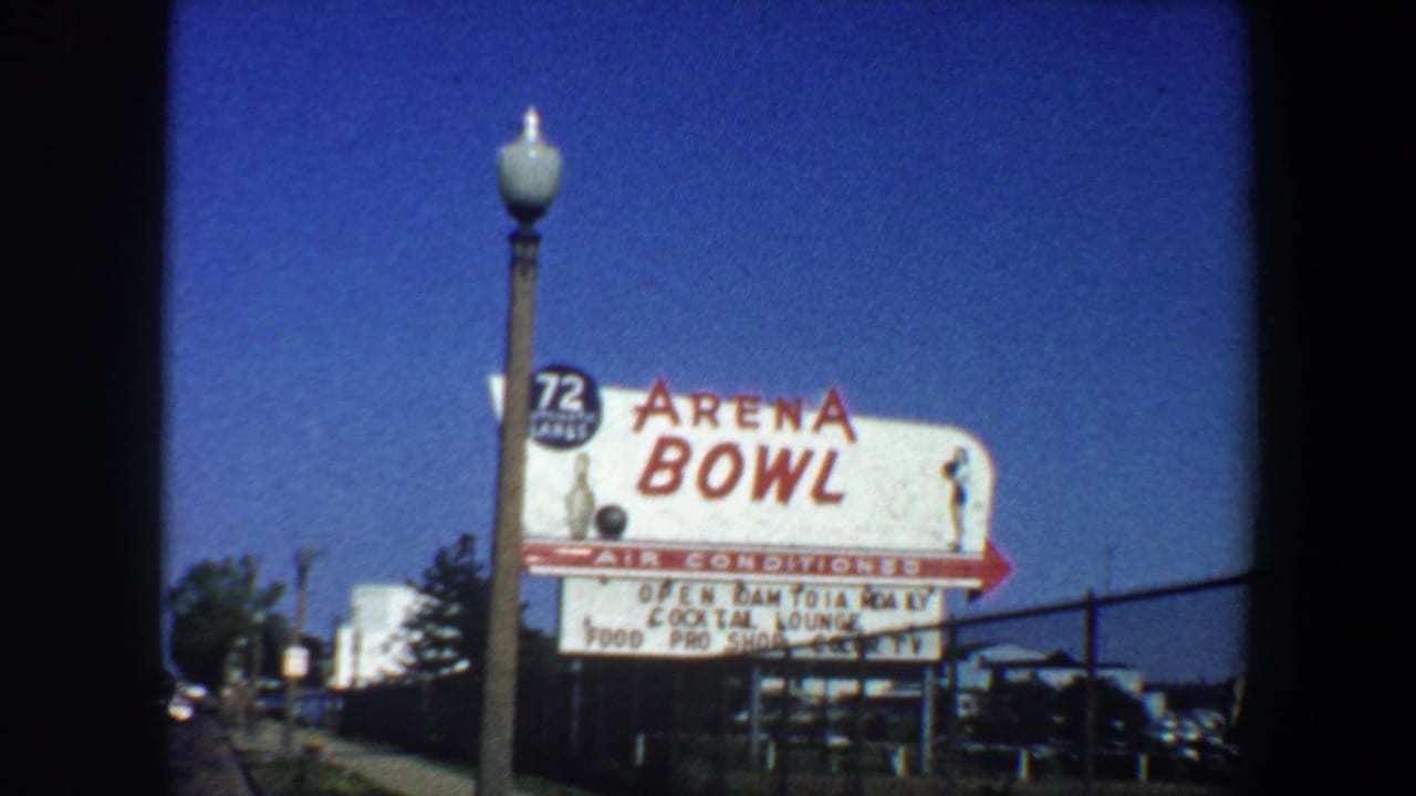 1964 St. Louis home-movie frame showing the Arena Bowl sign, sidewalk, streetlight, fence, and deep blue sky.