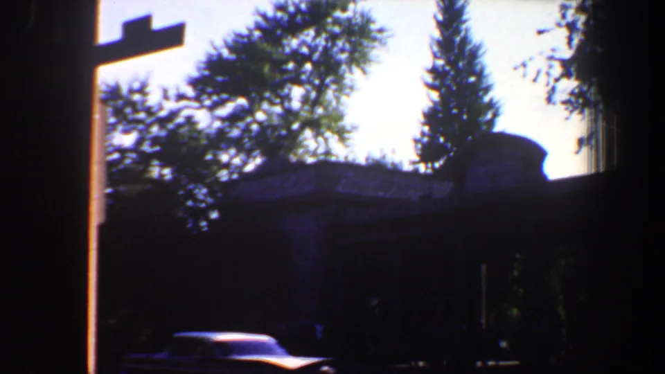 1964 Saint Louis street frame with silhouetted trees, a dark structure, and a partially visible parked car in low light.