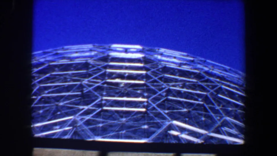 1964 Saint Louis frame with a centered metal lattice dome and stair-like horizontal bands beneath a saturated blue sky.