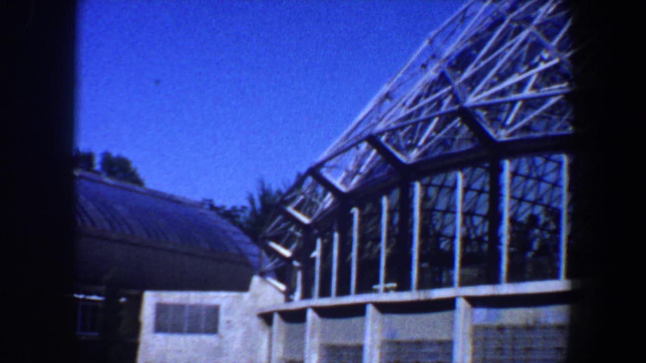Glass-roofed structure beside a smaller building and trees.