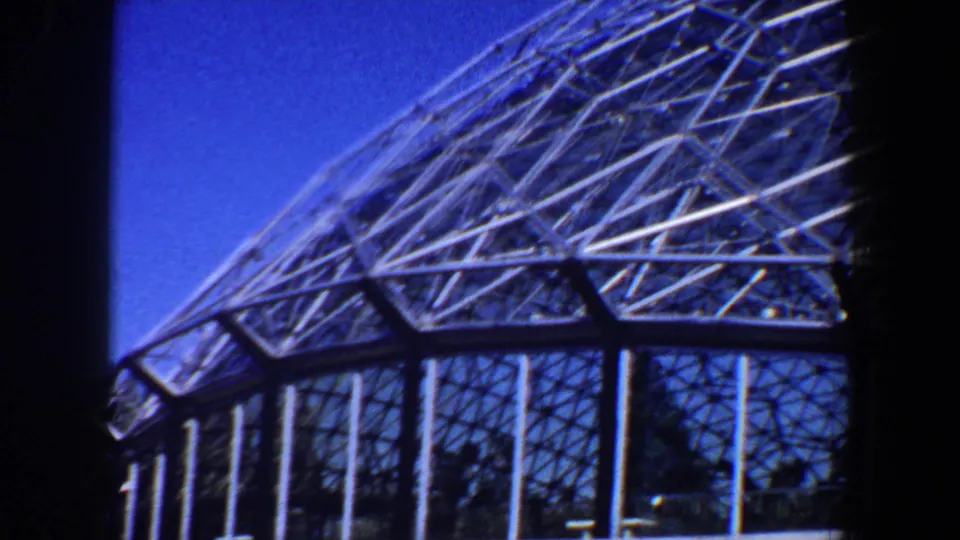 Saint Louis 1964 home-movie frame showing the glass wall and diagonal metal lattice of the large circular structure.